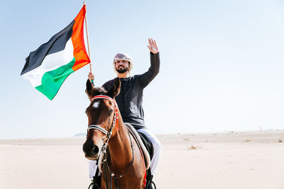 Man holding flag while riding horse at dessert