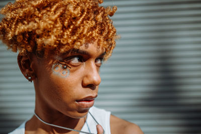 Multiracial charismatic teenager with creative makeup at his face standing at the street and posing