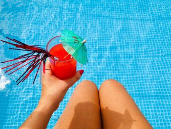 Midsection of woman holding drink while sitting by swimming pool