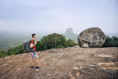 Side view of backpack man standing on cliff against sky