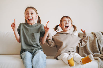 Funny happy two children girls sisters having fun on couch at home