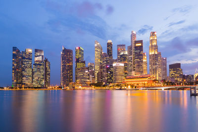 Illuminated modern buildings by bay against sky