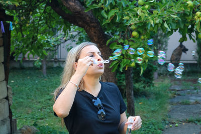 Mature woman blowing bubbles while standing outdoors