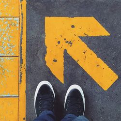 Low section of man standing by orange arrow symbol on walkway