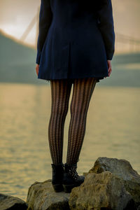 Low section of woman wearing stockings while standing on rock by river