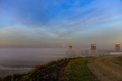 Scenic view of road by field against sky during foggy weather