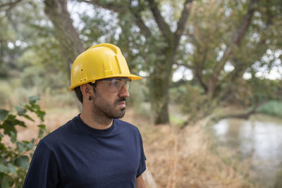 Man wearing hard hat standing against trees
