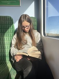 Portrait of young woman sitting on train reading major of carter bridge 