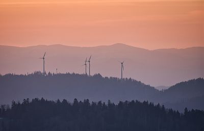 Scenic view of silhouette mountains with wind power plant against sky during sunset