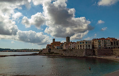 Buildings by sea against cloudy sky