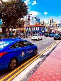 Cars on city street by buildings against sky