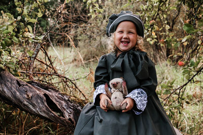 Full length of girl sitting with toy animal on branch