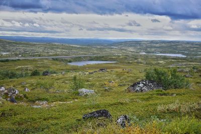 Scenic view of green landscape and mountains against cloudy sky