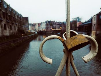Close-up of rusty metal by river in city against clear sky