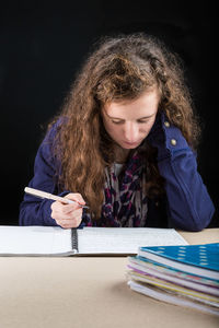 Young woman studying at desk against black background