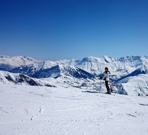 Full length of person skiing on snow covered field by mountains against clear blue sky