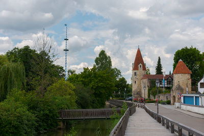 Footbridge amidst trees and buildings against sky