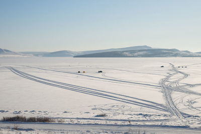 Winter lake with fishermen and traces of cars in the snow, against the background of mountains.