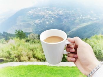 Close-up of woman holding coffee cup against mountain