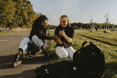 Smiling female friends using smart phone sitting in park