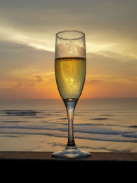 Wineglass on beach against sky during sunset