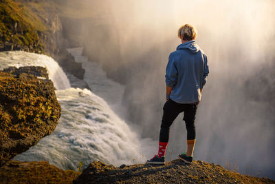 Rear view of man standing on rock against waterfall