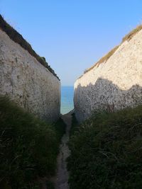 Footpath by sea against clear blue sky