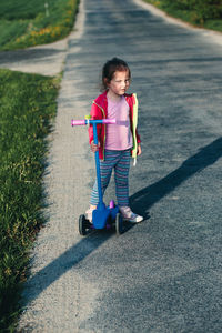 Portrait of cute girl with push scooter standing on road