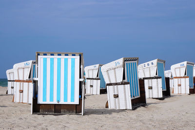 Hooded chairs at sandy beach against sky