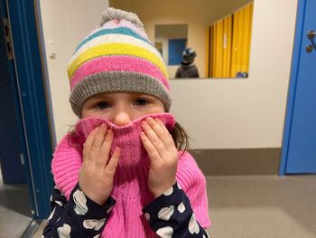 Portrait of a toddler girl wearing a colourful hat and scarf indoors