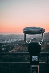 Close-up of coin-operated binoculars against cityscape during sunset