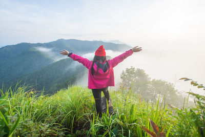 Woman with arms outstretched standing on mountain against sky