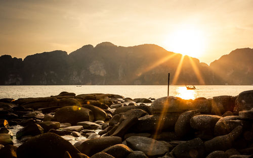 Rocks at sea shore against sky during sunset