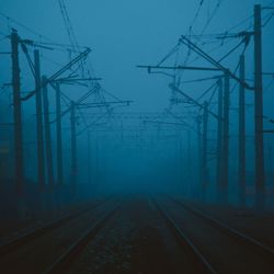 Railroad tracks amidst pylons against sky during foggy weather