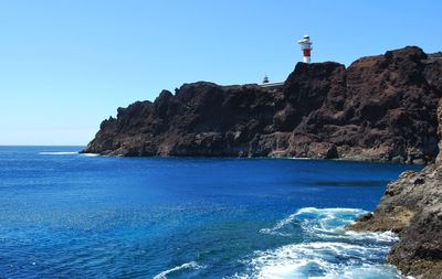 View of lighthouse in sea against clear blue sky