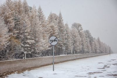 Road sign by snow covered trees against sky