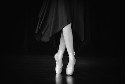 Low section of woman tiptoeing against black background