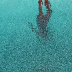 The shadow of a person seen on a stretch of sand that is wet by sea water