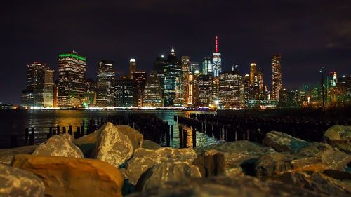 Illuminated modern buildings by river against sky at night