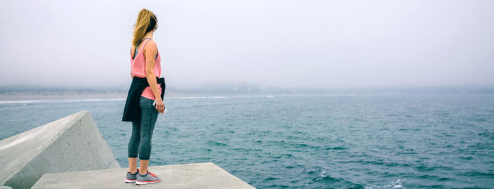 Rear view of woman standing by sea against sky