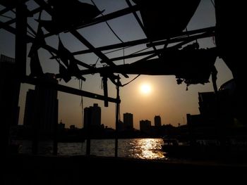 Silhouette buildings by river against sky during sunset