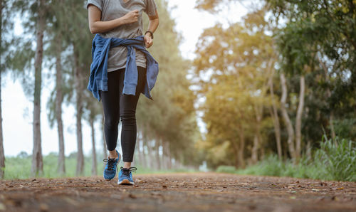 Low section of woman running on road amidst forest