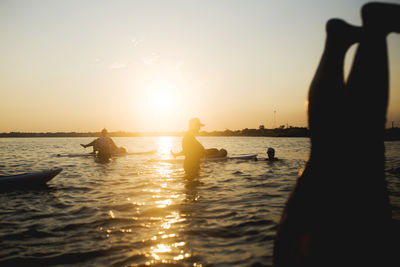 Silhouette people exercising on paddleboard in sea against sky