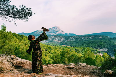 Woman with arms raised on mountain against sky