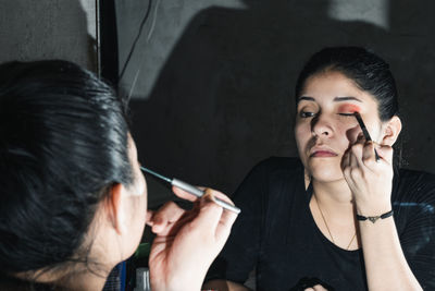 Beautiful latin woman in front of the mirror, applying red eye shadow with a small brush