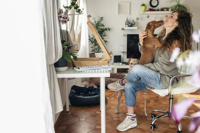 Painter sitting with pet dogs on chair in living room at home