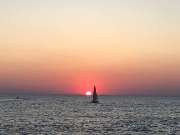 Sailboat sailing on sea against romantic sky at sunset