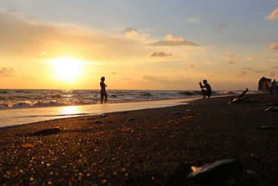 Silhouette people on beach against sky during sunset