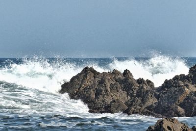 Waves splashing on rocks at shore against sky