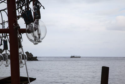 Light bulbs hanging on pole by sea against sky